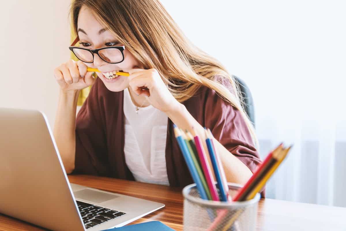 stressed woman in glasses looking at laptop and biting a pencil