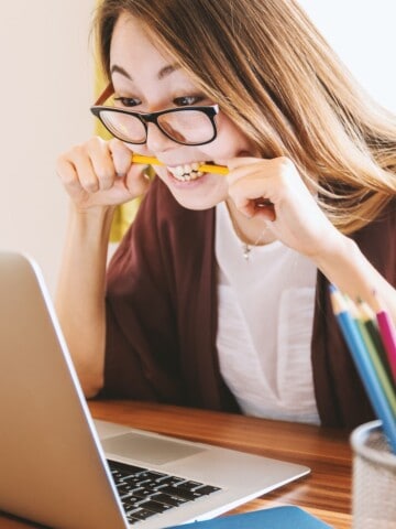 stressed woman in glasses looking at laptop and biting a pencil