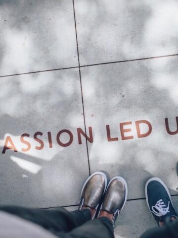 Passion led us quote next to 2 pairs of feet on sidewalk.